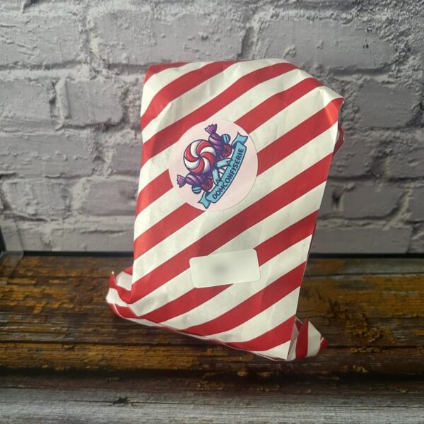 Sachet emballé dans un papier rayé rouge et blanc, fermé par l'autocollant DomConfiserie